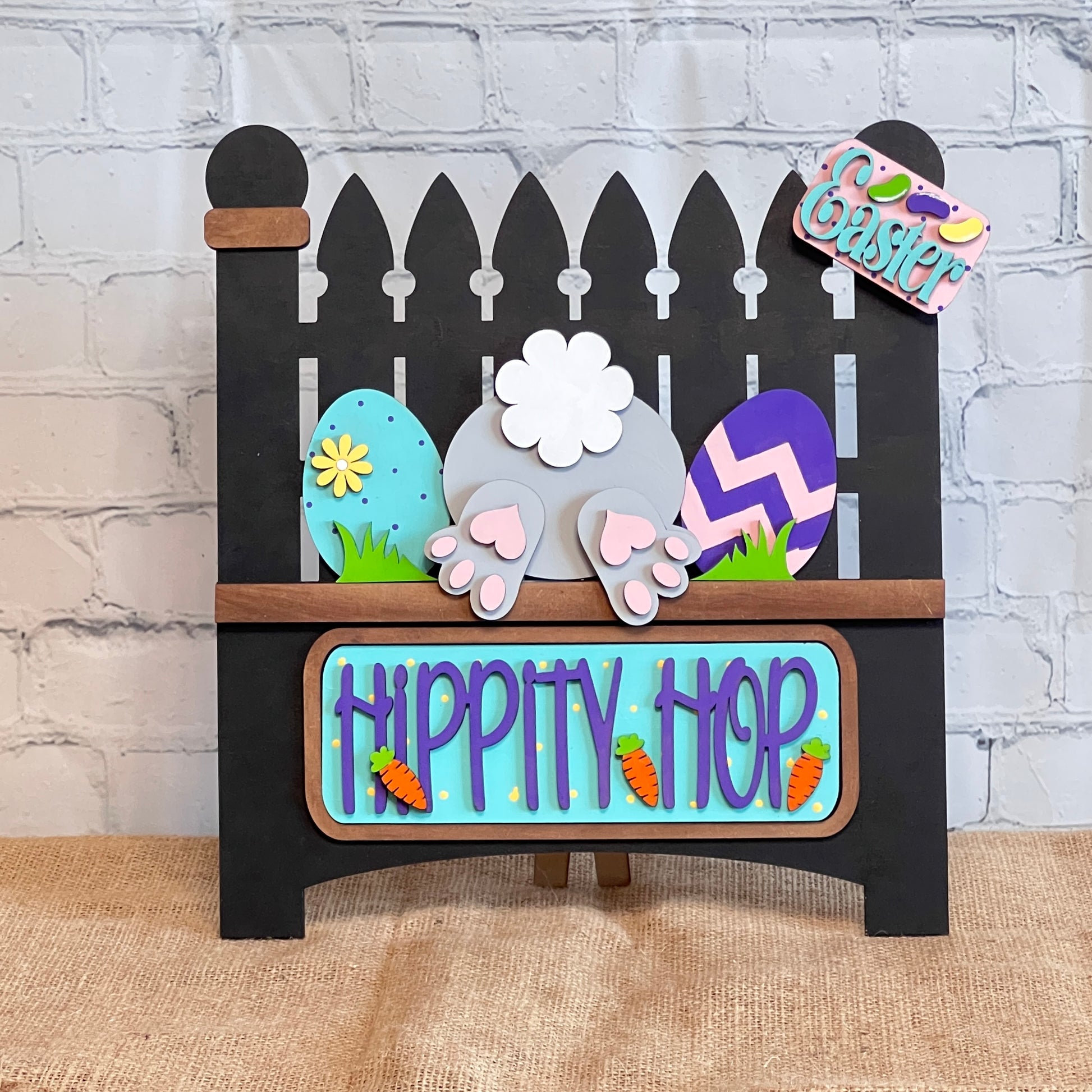 Janet's Craft Corner offers a charming DIY home decor kit featuring a bunny bottom, colorful eggs, a "Hippity Hop" sign with carrots, and an "Easter" tag on burlap. This Garden Fence with Insert includes a black picket fence and interchangeable inserts for endless creativity.