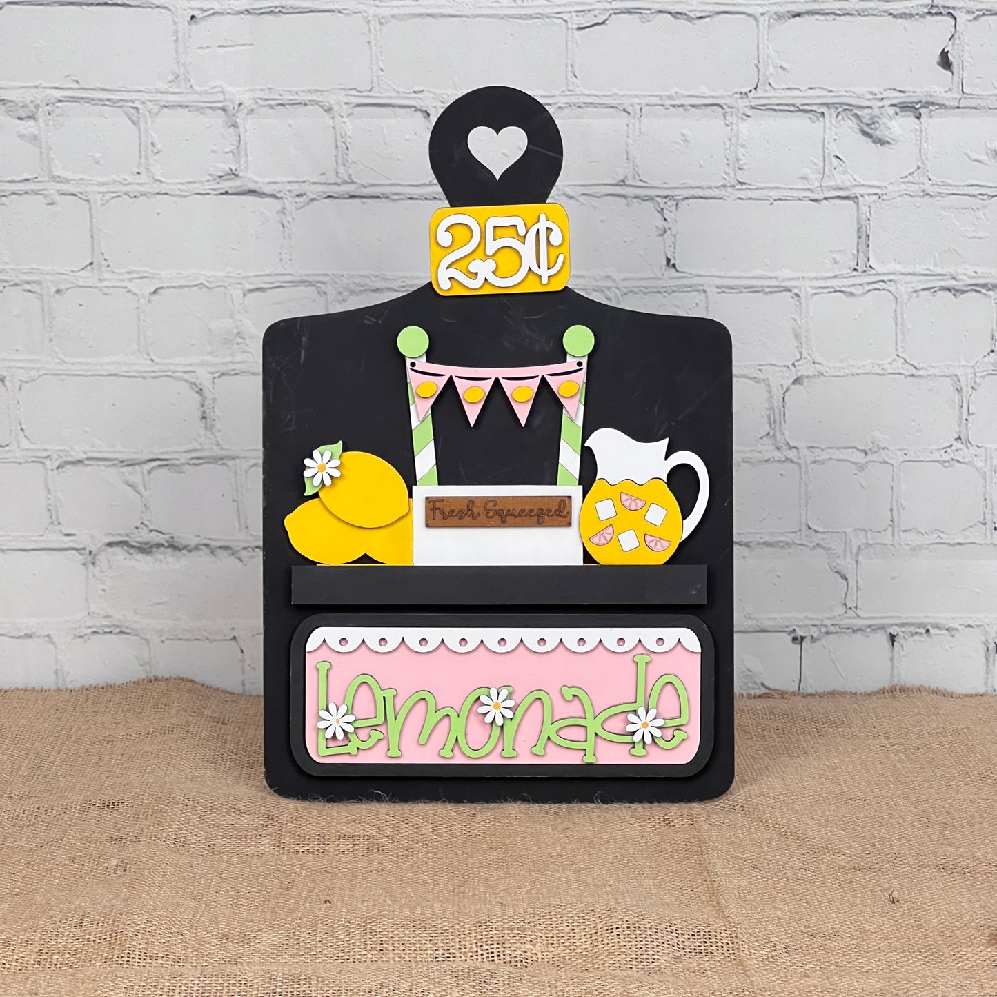 Janet's Craft Corner offers a Breadboard Interchangeable Base with Insert, featuring a 25¢ lemonade theme with pitcher, lemons, Fresh Squeezed label, pastel bunting, and daisies. A perfect DIY home decor kit for enthusiasts with changeable pieces to tailor your display.