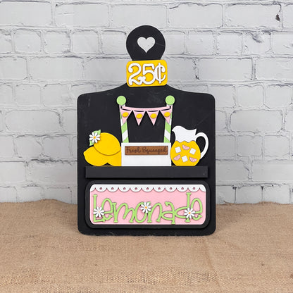 Janet's Craft Corner offers a Breadboard Interchangeable Base with Insert, featuring a 25¢ lemonade theme with pitcher, lemons, Fresh Squeezed label, pastel bunting, and daisies. A perfect DIY home decor kit for enthusiasts with changeable pieces to tailor your display.