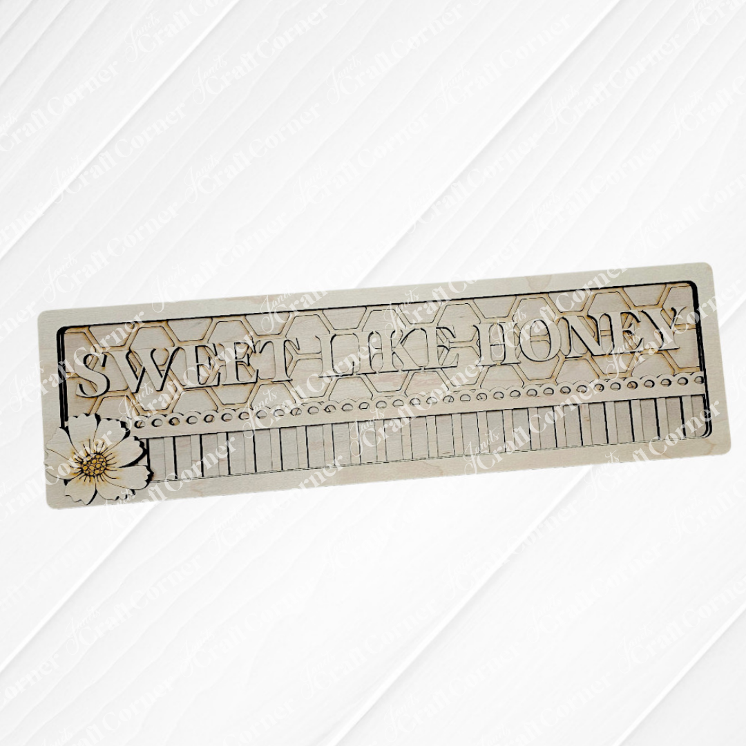 The Sweet Like Honey Chunky Shelf Sitter by Janet's Craft Corner is a decorative rectangular sign featuring "Sweet Like Honey" in large letters, a honeycomb background, and a sunflower illustration in the lower left corner. Perfect for shelf decor or DIY craft kit lovers with its intricate wood cut-outs.