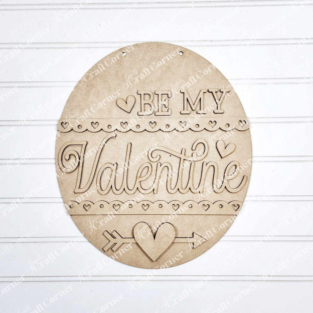 Janet's Craft Corner presents the "Be My Valentine Door Hanger," a chic DIY home decor kit featuring a round, wooden design with hearts, an arrow, and elegant engraving on a white wood-paneled background.