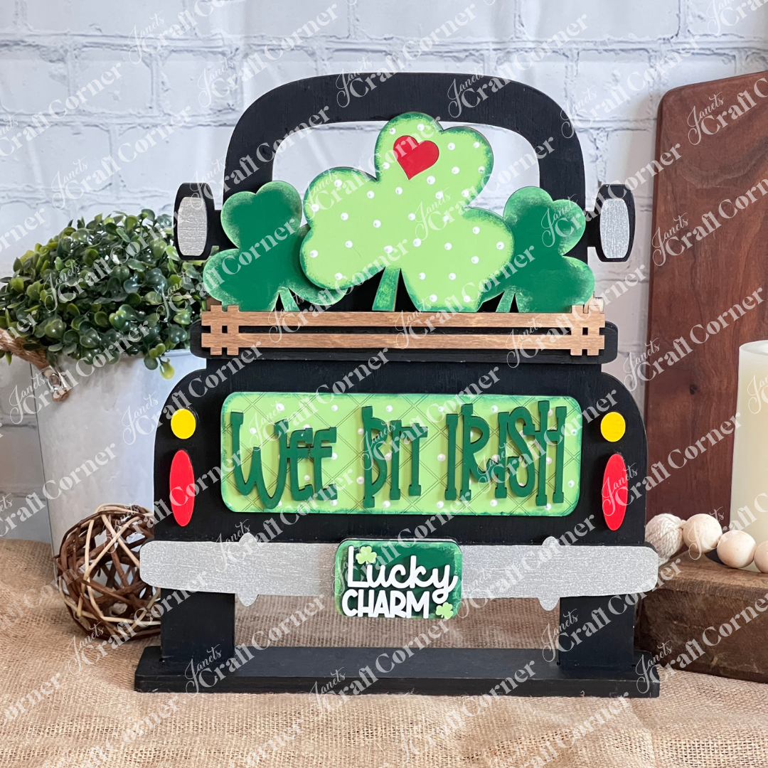 Janet's Craft Corner presents the "Wee Bit Irish Interchangeable Insert," a decorative sign highlighting Irish pride with a black truck, shamrocks, and license plate reading "Lucky Charm," set against a light brick wall. Perfect for your DIY craft kit collection.