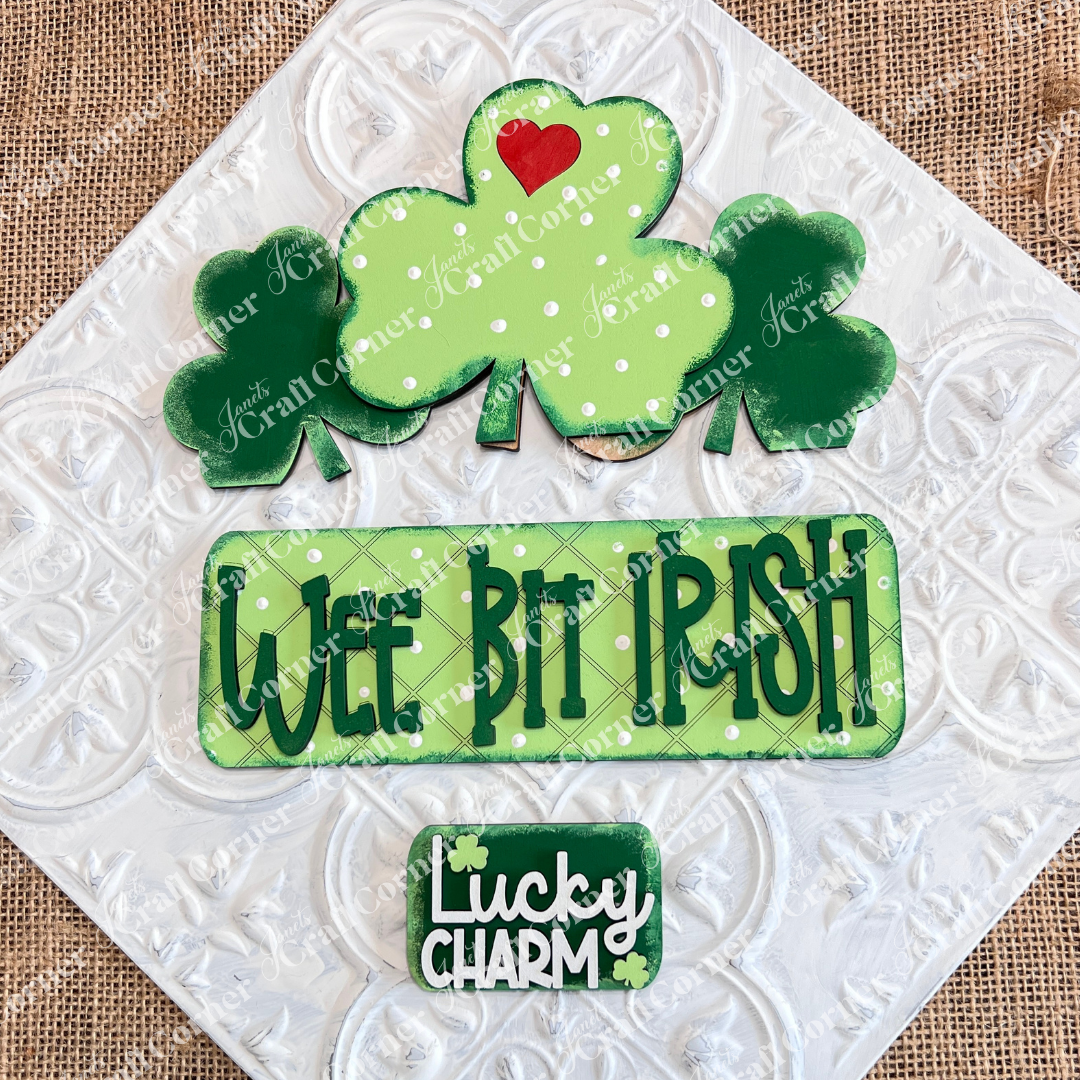 The "Wee Bit Irish Interchangeable Insert" by Janet's Craft Corner features cookies with green shamrocks and a red heart, ideal for displaying Irish pride. Text cookies say "Wee Bit Irish" and "Lucky Charm" on a burlap backdrop.