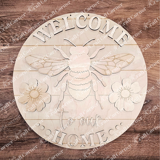 The Welcome Home Bees & Blooms Door Hanger by Janet's Craft Corner is a charming DIY project featuring a carved bee with flowers, encircled by "WELCOME to our HOME" text on rustic wood grain, perfect for craft enthusiasts.