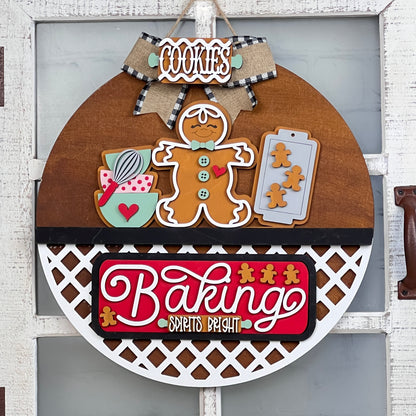 Adorn your door with Janet's Craft Corner's charming DIY interchangeable base and insert. This round wooden sign features a gingerbread man, baking utensils, cookie trays, plaid ribbon, and reads "Baking Spirits Bright," adding festive flair to any entrance.