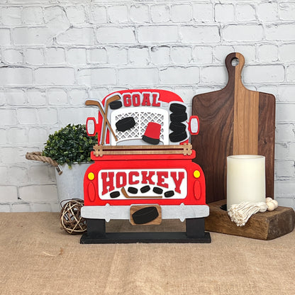 Crafted by Janet's Craft Corner, this DIY interchangeable home decor kit features an antique truck base and insert, displaying "Goal" and "Hockey" text with sticks and pucks. Ideal for home decoration, it pairs beautifully with plants and cutting boards.