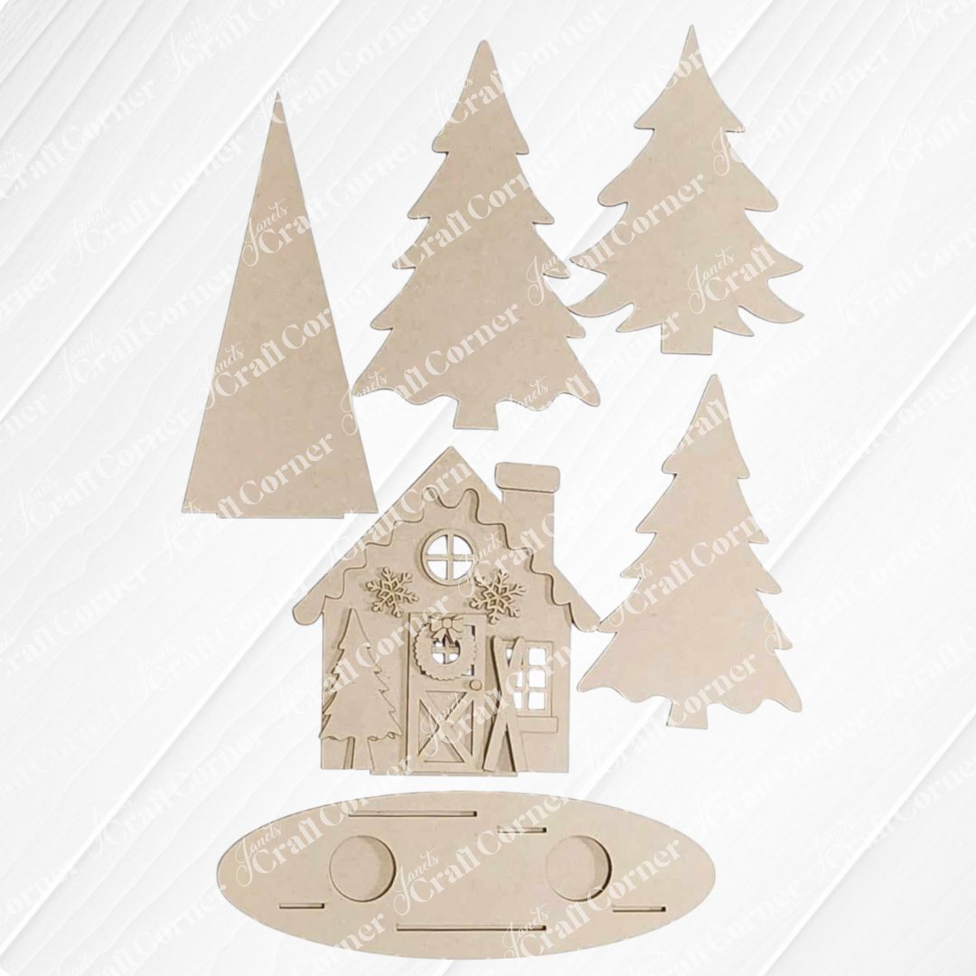 Flat lay of the unassembled Winter Cabin Votive Holder by Janet's Craft Corner, featuring wooden cutouts of a winter cabin, trees, and an oval base. The cottage boasts intricate window and door designs. Each piece is crafted to fit together as part of a handmade home decor or DIY craft kit project.