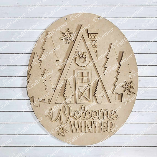 The Winter Cabin Wall Hanger by Janet's Craft Corner is a delightful circular wooden plaque featuring a carved A-frame house surrounded by trees and snowflakes, along with the phrase "Welcome Winter." The light wooden background enhances its charm, making it an ideal addition to any DIY craft kit for home décor.