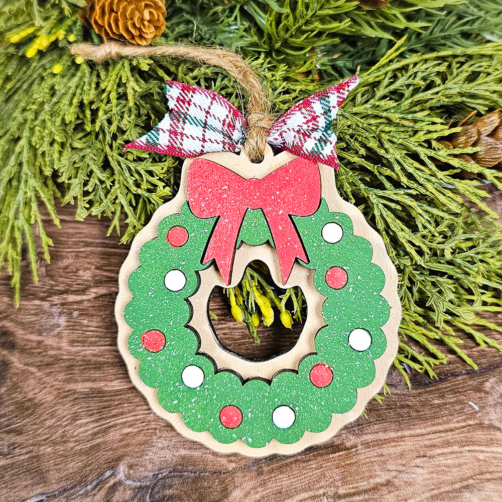 The Sugar Cookie Ornaments - Set of 3 by Janet's Craft Corner offers a charming DIY decoration kit that includes three wooden Christmas ornaments, each shaped like a wreath. They are beautifully adorned with green glitter, red circles, and white dots. A red bow adorns the top of each ornament, tied with a plaid ribbon. These personalized home décor pieces elegantly rest on a wooden surface with greenery in the background.