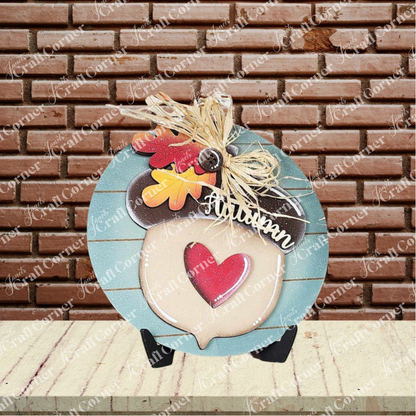 Janet's Craft Corner Fall Harvest Mini Shelf Sitters DIY kit features a round blue wooden "Autumn" sign with leaves, raffia bow, and red heart—perfect for seasonal home decor or creative crafting.
