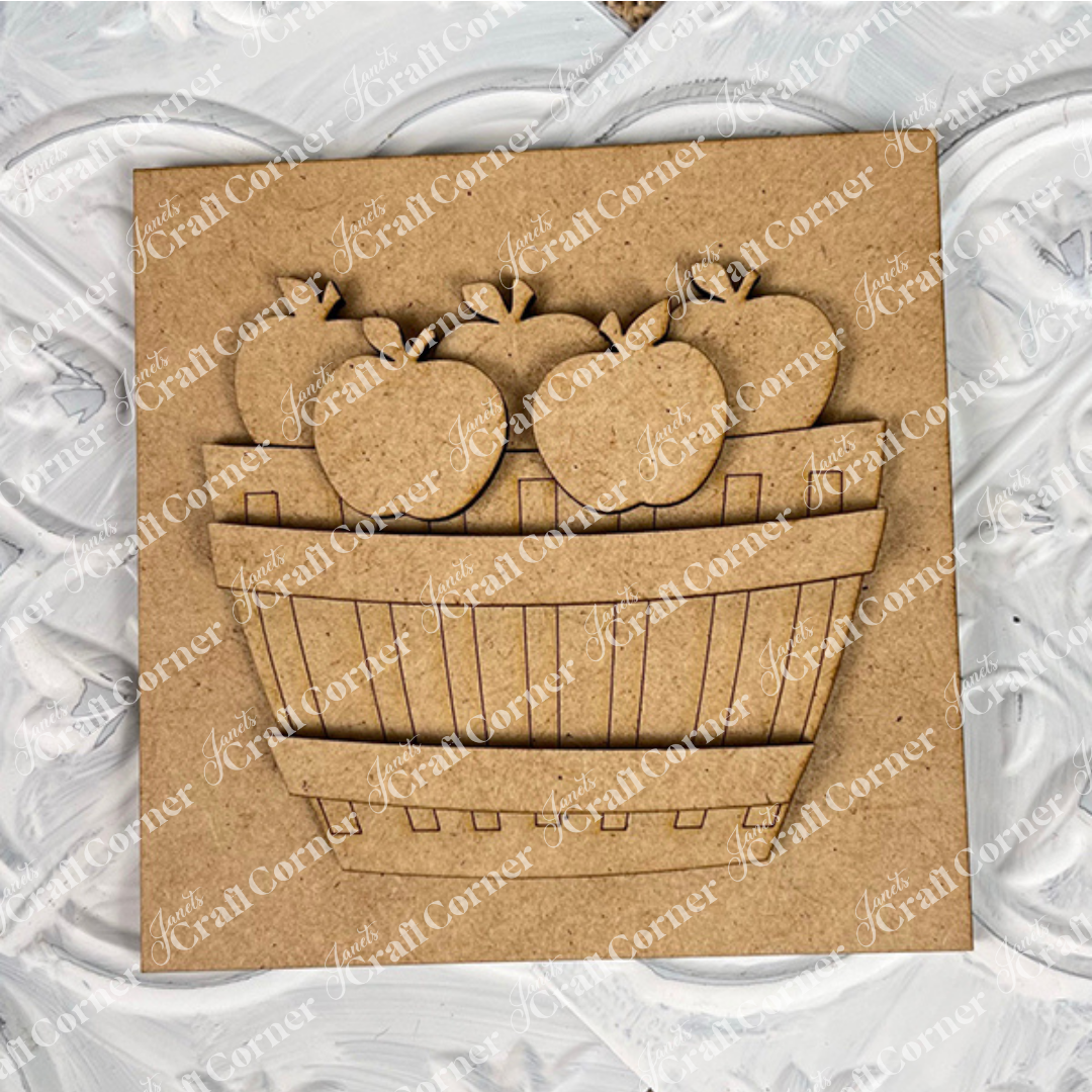 Janet's Craft Corner Apple Basket Square features a square wood piece with a raised, laser-cut basket of five apple cut-outs on a textured, painted white background—ideal unfinished DIY home decor.