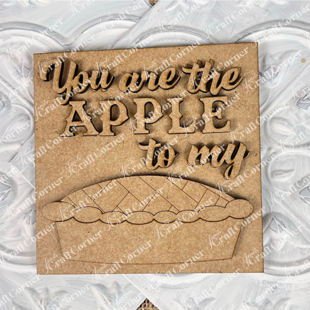 Janet's Craft Corner apple pie square features a wooden sign with raised "You are the apple to my" lettering and a pie cut-out—perfect for DIY seasonal home decor, displayed on a painted white textured surface.