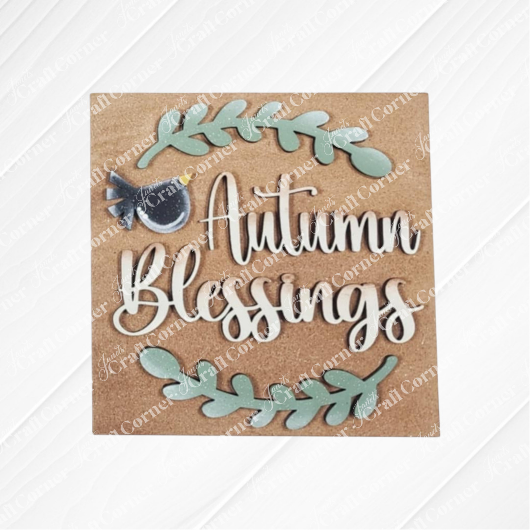 The "Fall Scarecrow Squares" sign by Janet's Craft Corner displays "Autumn Blessings" in white script with green leafy branches and a small blue bird on a brown background—ideal for seasonal home decor.