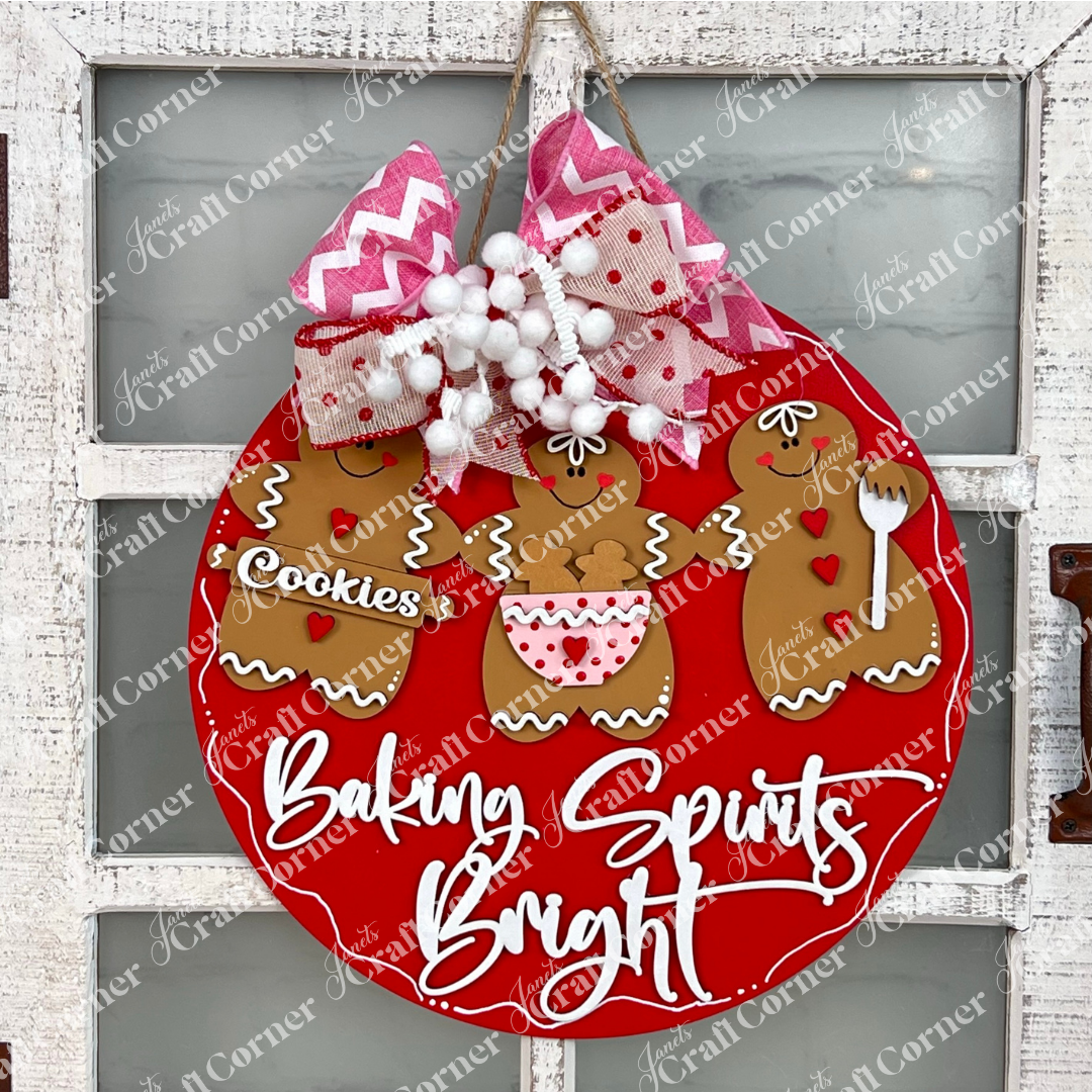 Janet's Craft Corner's Baking Spirits Bright Wall Hanger DIY kit features festive gingerbread figures, a pink and red bow, and cheerful script—perfect seasonal decor for any white rustic wall. Set of 1.