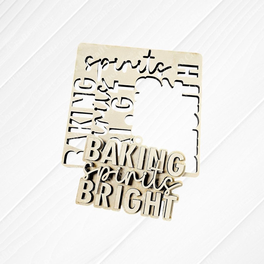 A wooden cutout from the Baking Spirits Bright Ornaments - Set of 4 by Janet's Craft Corner features the phrase "BAKING spirits BRIGHT" in bold letters, with "spirits" elegantly scripted in cursive. It sits on a wooden surface alongside its original frame, making it a charming addition to your holiday decor.