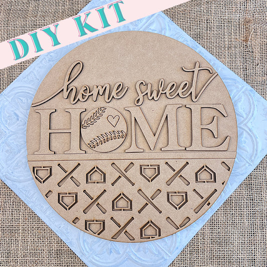 Introducing the "Baseball Home Sweet Home Round" from Janet's Craft Corner. This round wooden DIY sign showcases the phrase "home sweet HOME" along with a baseball door hanger design. The bottom half features intricate cut-out patterns set against a burlap background, and the kit conveniently includes "DIY KIT" labeled in the corner.