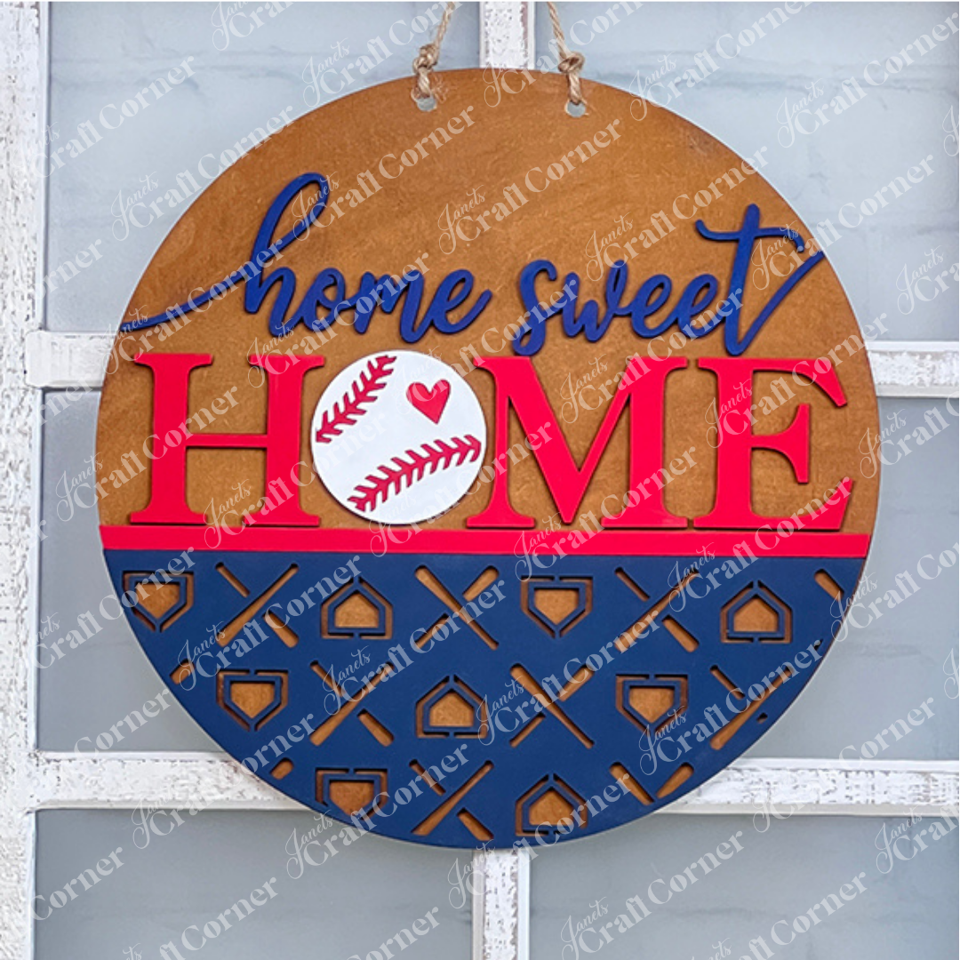 Crafted by Janet's Craft Corner, the Baseball Home Sweet Home Round is a round wooden door hanger featuring "home sweet HOME" emblazoned in blue and red. The "O" in "HOME" is cleverly designed as a baseball with a red heart, accented by a striking blue pattern. This delightful piece of home decor hangs elegantly by rope against a glass window and is an ideal addition for any DIY kit enthusiast.
