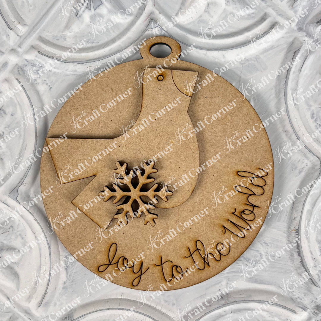 Introducing Janet's Craft Corner's Round Christmas Ornaments from the DIY Decoration Kits! This delightful wooden ornament is shaped like a bird and adorned with a snowflake, featuring "joy to the world" engraved on it. It's beautifully complemented by a textured white background, making it a charming addition to your holiday decor.