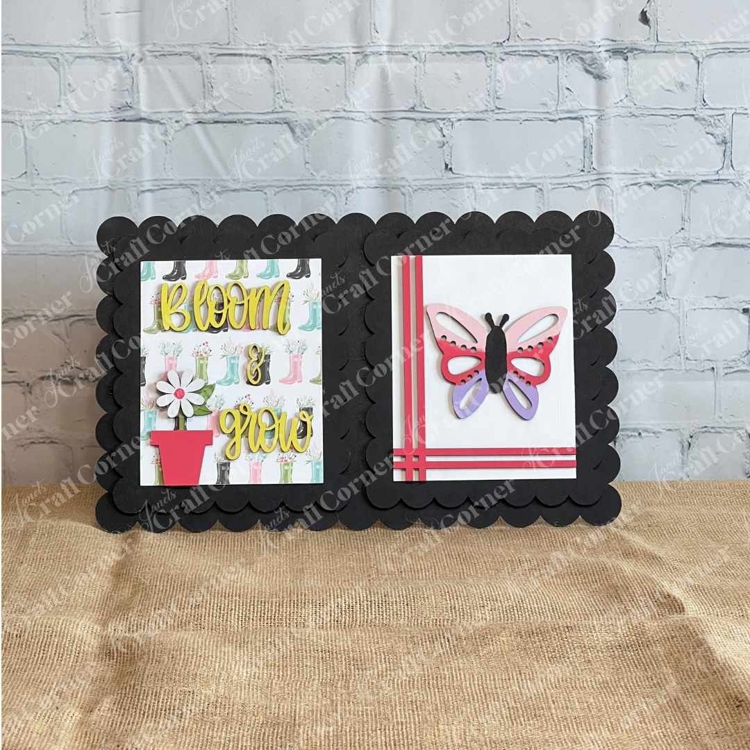 Two handmade cards from Janet's Craft Corner are displayed on a black scalloped board: one reads "Bloom & Grow" with a flowerpot, the other has a 3D butterfly and red stripes—ideal for styling with the Spring Switchable Farmhouse Signs DIY kit.