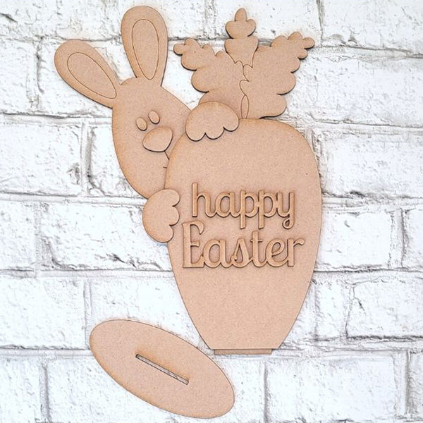 Enhance your Easter decor with Janet's Craft Corner's Bunny and Carrot Happy Easter Shelf Sitter—a charming kit featuring a bunny peeking from behind a carrot engraved with "happy Easter," against a white brick backdrop.