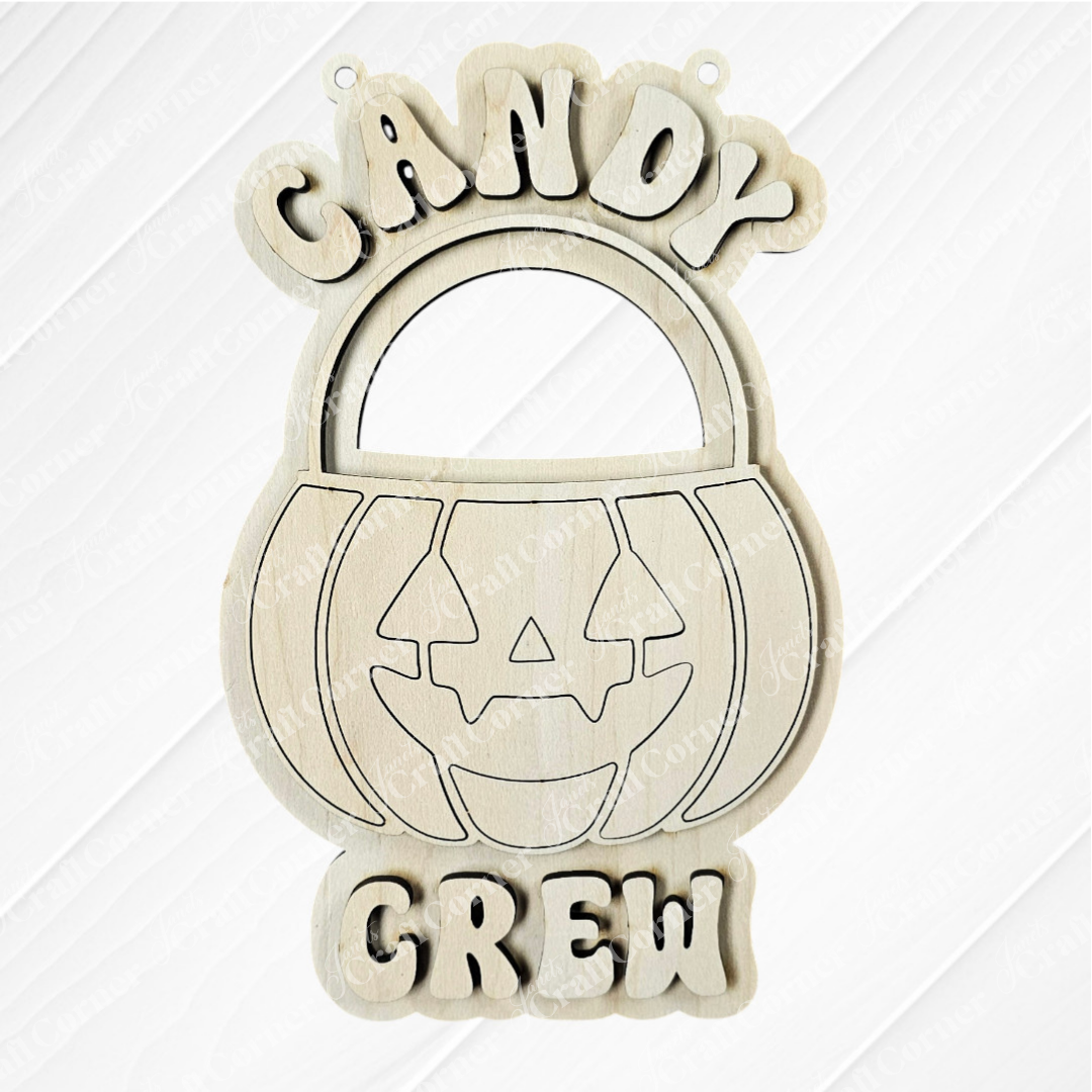 Janet's Craft Corner’s Candy Crew Kids Pop-Out is a wooden Halloween pumpkin bucket decor with a jack-o’-lantern face and “CANDY CREW” text above and below.