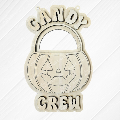Janet's Craft Corner’s Candy Crew Kids Pop-Out is a wooden Halloween pumpkin bucket decor with a jack-o’-lantern face and “CANDY CREW” text above and below.
