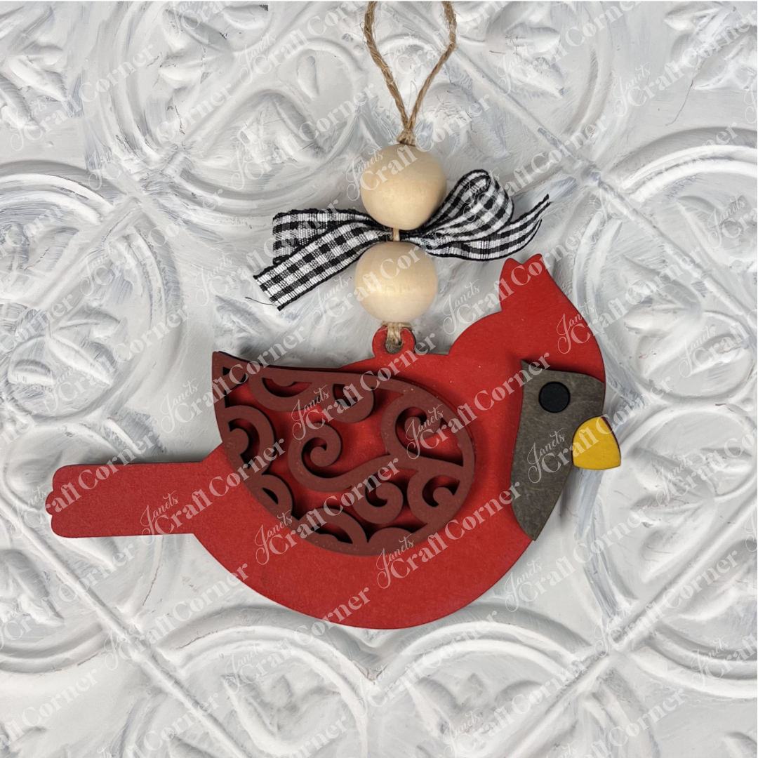 The Cardinal Ornament from Janet's Craft Corner DIY Decoration Kits captures the essence of festive holiday décor with its intricate designs, vibrant red color, hanging string adorned with two wooden beads, and a black-and-white checkered bow. Set against a textured white background, it's the perfect touch for any seasonal setting.