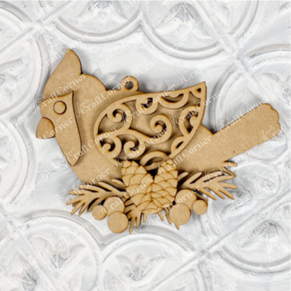 This elegant ornament from Janet's Craft Corner's DIY Decoration Kits showcases a cardinal with detailed scrollwork on its wing, poised atop pinecones and branches. Ideal for holiday décor, it stands out wonderfully against a textured white background.