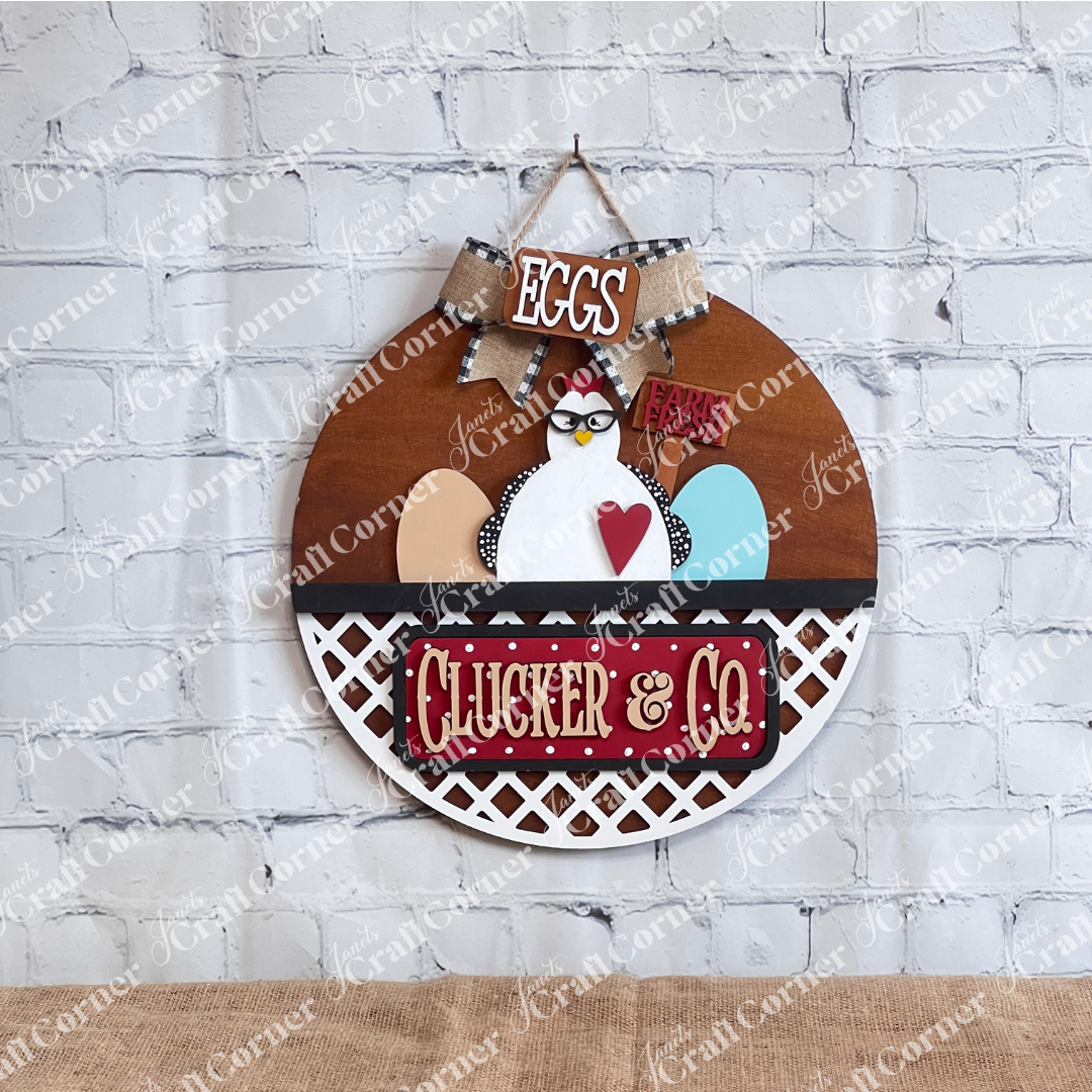 Janet's Craft Corner introduces the Clucker & Co. Interchangeable Insert - Painted, a decorative piece featuring a delightful chicken motif adorned with glasses, alongside a red heart and colorful eggs. The sign displays "EGGS" and "Farm Fresh" at the top, with "Clucker & Co." beneath on a rustic lattice background, making it an ideal choice for farmhouse decor enthusiasts seeking versatile craft inserts.