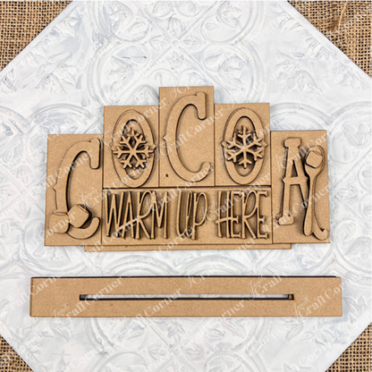 The Cocoa Mini Word Block by Janet's Craft Corner features "COCOA WARM UP HERE" with snowflakes, a mitten, and a mug on a textured white background. This hand-painted wooden sign is perfect for cozy home décor.