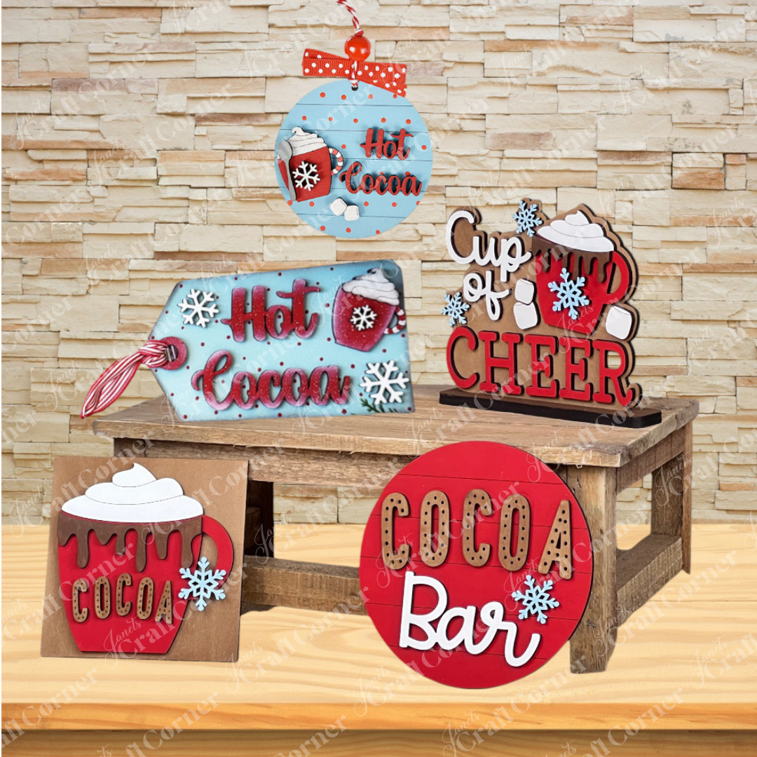Add cozy winter charm to your home with Janet's Craft Corner Hot Cocoa Mini Shelf Sitters, a DIY seasonal decor kit featuring cocoa-themed designs, perfect for displaying on a bench or shelf against a stone wall backdrop.