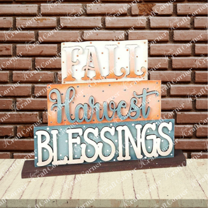 The Fall Harvest Mini Shelf Sitters DIY craft kit by Janet's Craft Corner features a wooden sign with “FALL Harvest BLESSINGS” in white, orange, and blue—perfect autumn decor for your space or a charming addition to any shelf display.