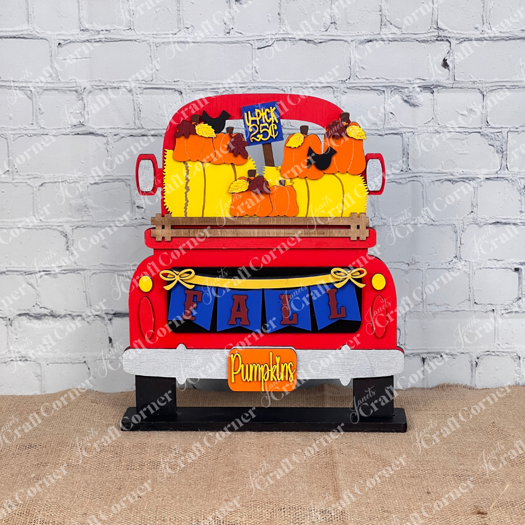 Decorative fall-themed truck with pumpkins and corn stalks against a white brick wall.
