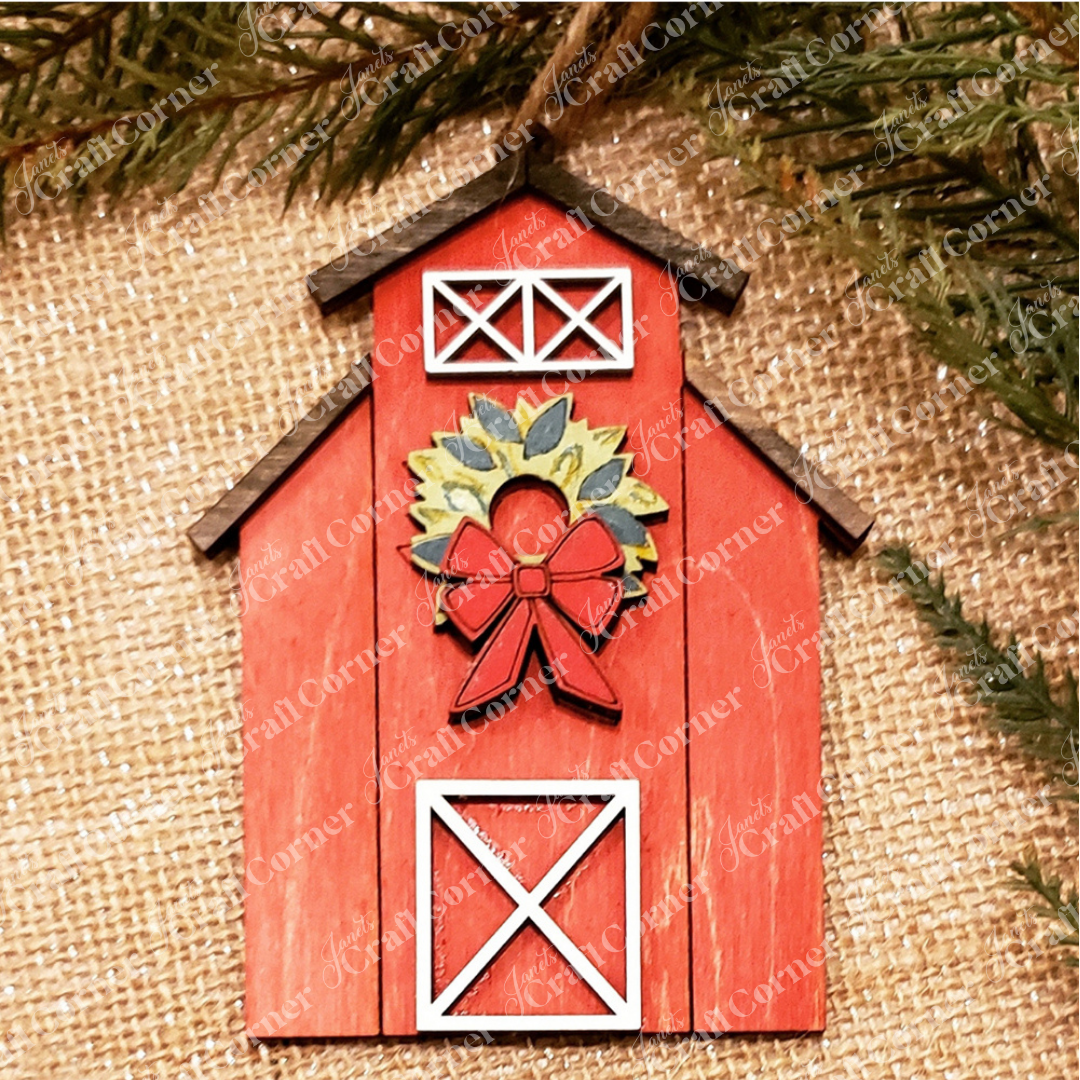 A festive red barn with white trim and a holiday wreath hangs on burlap with pine branches—a charming addition to Janet's Craft Corner Farm Life Christmas Ornaments DIY seasonal craft kit (choice of 4).