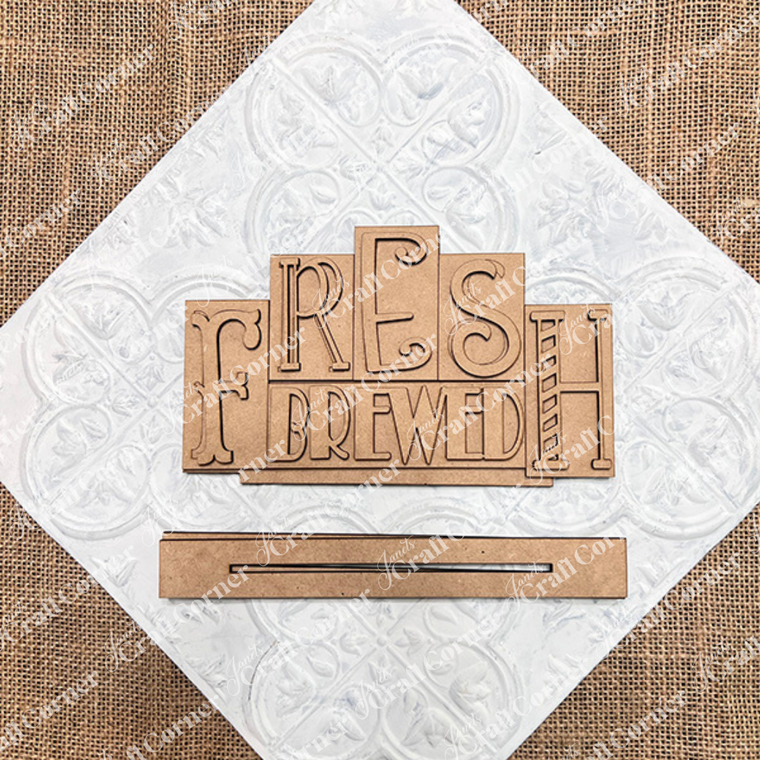 The "Fresh Brewed Mini Word Block Shelf Sitter" from Janet's Craft Corner features wooden letters on a white and burlap backdrop, ideal for coffee enthusiasts. 