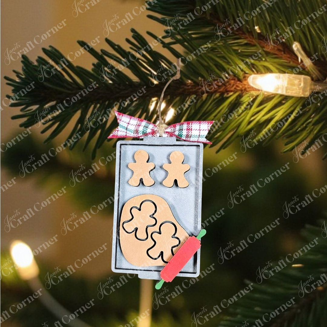 A festive scene with gingerbread men and clover shapes on a baking tray, surrounded by greenery and a plaid ribbon. A small red rolling pin is placed nearby on a wooden surface, reminiscent of crafting your own Janet's Craft Corner Baking Spirits Bright Ornaments - Individual Painted DIY kit.
