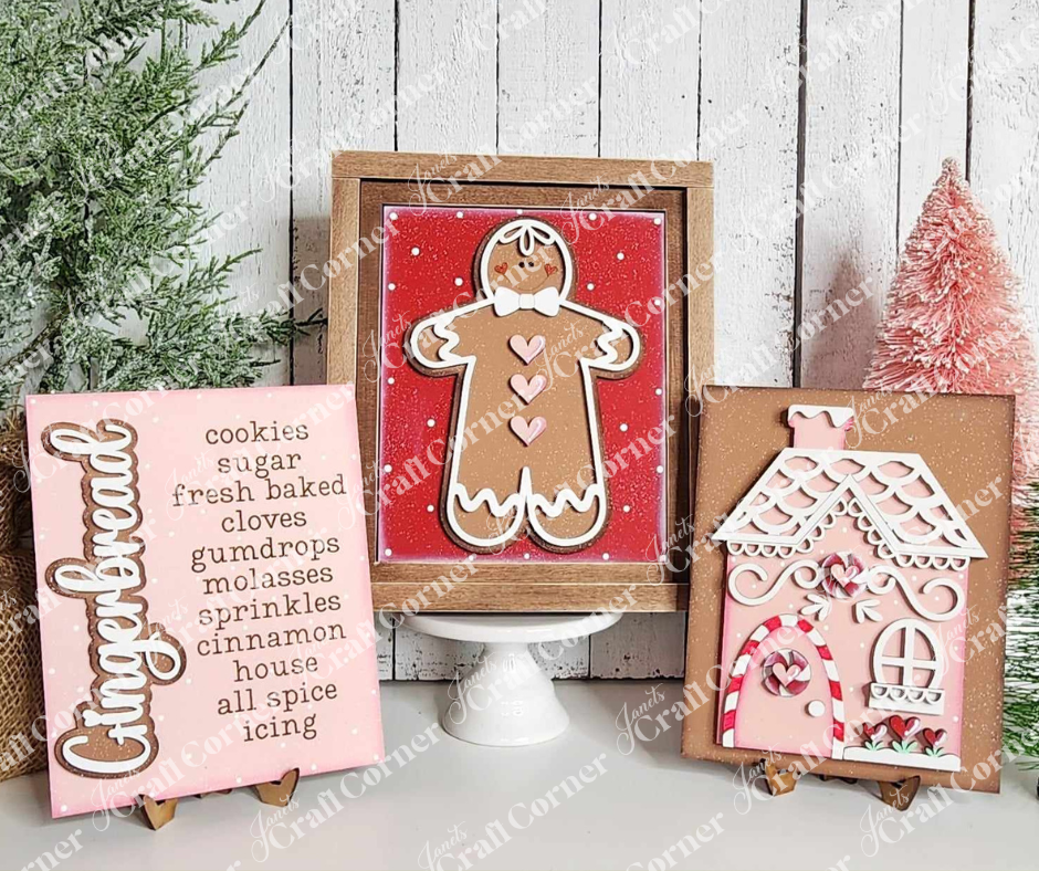 Three festive signs are displayed in Janet's Craft Corner's Farmhouse Frame for Interchangeable Signs: one lists gingerbread ingredients, another features a gingerbread person, and the third shows a gingerbread house. Pine trees and snowy backgrounds add charming holiday decor to any space.