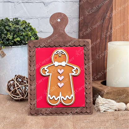 A decorative gingerbread figure with pink hearts sits on Janet's Craft Corner's Bead Trim Breadboard Frame for Switchable Farmhouse Signs—an ideal DIY seasonal home decor kit to add farmhouse charm to your space.