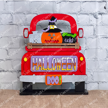 This delightful DIY home decor kit features Janet's Craft Corner's Halloween Pumpkin Interchangeable Insert, showcased on a truck with a cheerful pumpkin wearing a witch hat. The vibrant "HALLOWEEN" and "BOO!" text enhance its festive appeal. Accompanied by a plant, candle, and cutting boards set against a brick wall backdrop, it's ideal for those who enjoy interchangeable craft inserts.
