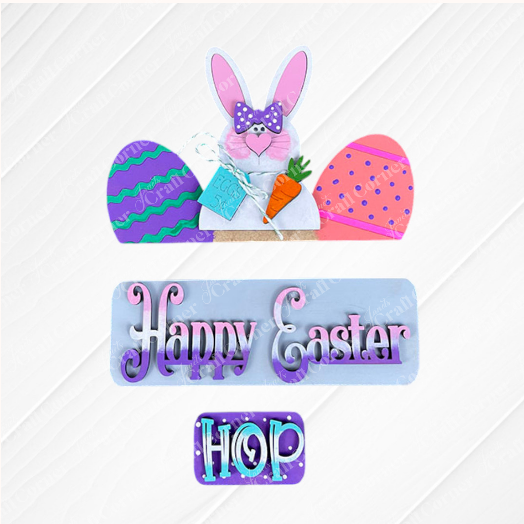 This interchangeable home decor kit from Janet's Craft Corner features a decorative Easter sign on burlap, displaying a pink-eared bunny clutching a carrot amidst colorful eggs. With text panels that say "Happy Easter" and "Hop," it adds vibrant charm to your space, making it perfect as an Easter Bunny insert for your seasonal displays.
