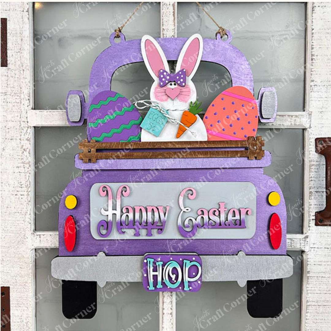 The Easter Bunny Interchangeable Insert from Janet's Craft Corner is a DIY home decor kit that features a charming purple truck adorned with an Easter Bunny sporting a polka dot bow tie and holding a carrot. The truck bed is filled with vibrant Easter eggs and includes a sign that reads "Easter 5¢." The license plate displays "HOP," while the back of the truck sends out cheerful "Happy Easter" wishes.