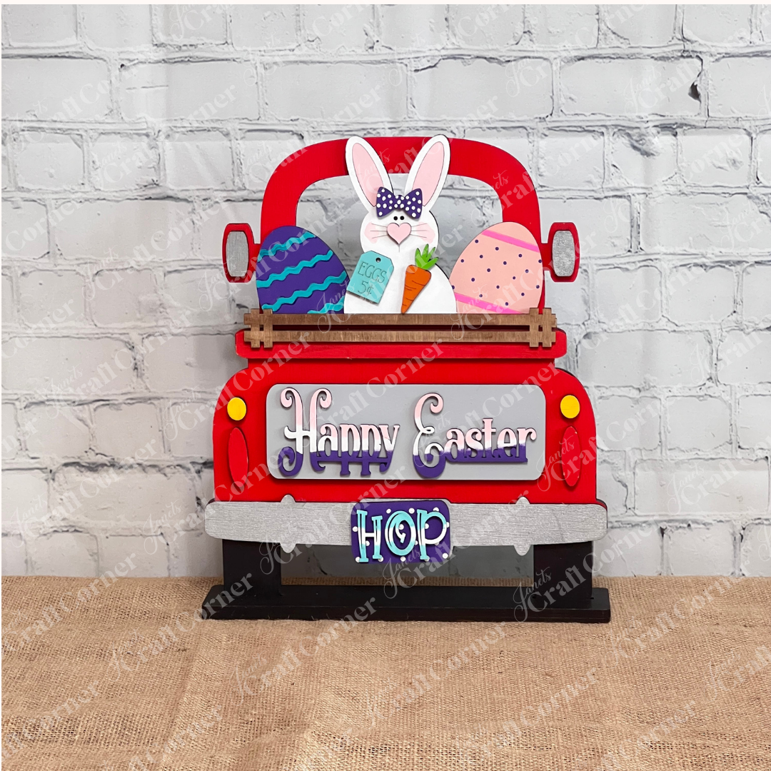 The Happy Easter Bunny Interchangeable Insert from Janet's Craft Corner is a DIY home decor kit with 3 pieces, featuring a truck with a bunny, colorful eggs, and carrot. Adorned with "Happy Easter" and "Hop," it's perfect against on a red antique truck.