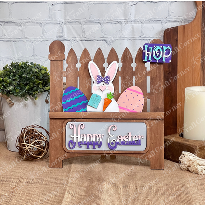 Janet's Craft Corner offers a DIY home decor kit: the Happy Easter Bunny Interchangeable Insert, featuring 3 pieces including a bunny with a carrot and "Eggs 5¢" sign, colorful eggs, and stylized "Happy Easter," all displayed on a stained garden fence base. Perfect for decorating against a brick wall backdrop.