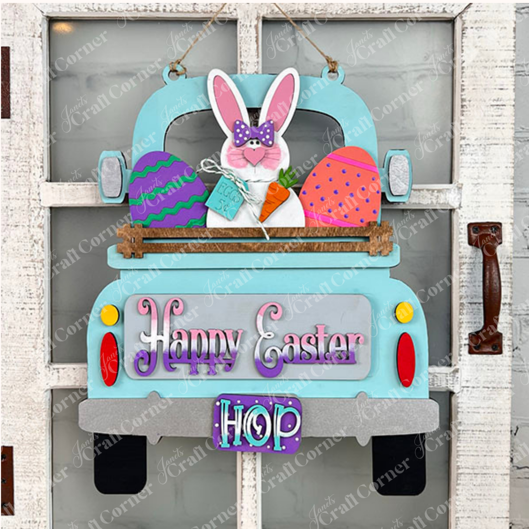 This charming Easter Bunny Interchangeable Insert from Janet's Craft Corner, an ideal DIY home decor kit, showcases a lively blue truck carrying a bunny, eggs, and a carrot. With "Happy Easter" and "Hop" embellishments, it beautifully adorns a rustic white door.
