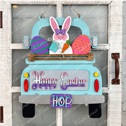 This charming Easter Bunny Interchangeable Insert from Janet's Craft Corner, an ideal DIY home decor kit, showcases a lively blue truck carrying a bunny, eggs, and a carrot. With "Happy Easter" and "Hop" embellishments, it beautifully adorns a rustic white door.