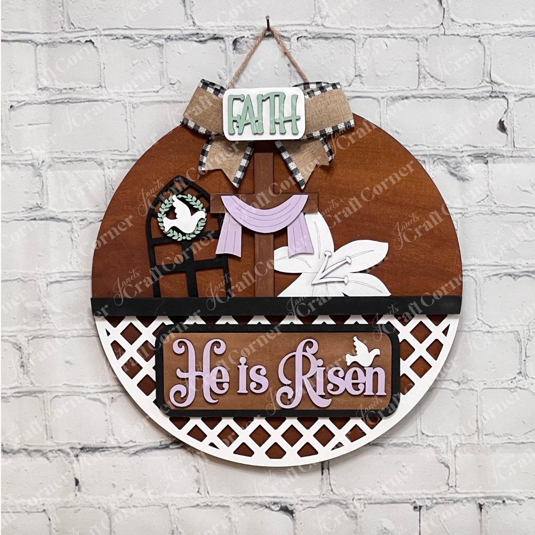 The "He is Risen Insert" from Janet's Craft Corner is a DIY home decor craft kit featuring a round wooden decoration with purple text, a cross, lilies, and "Faith" above it. It's perfect for an elegant Easter display against a white brick backdrop. Comes as 1 set of 3 pieces.