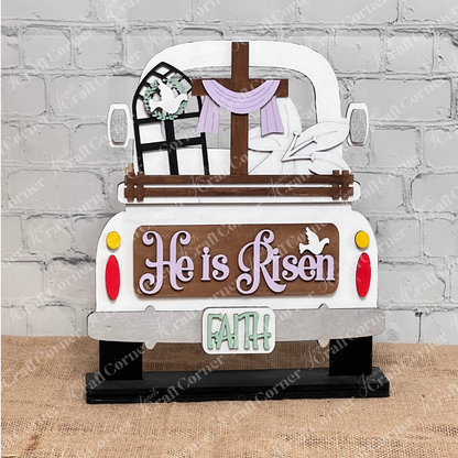 This DIY home decor kit from Janet's Craft Corner includes an interchangeable wooden decoration featuring the back of a truck with "He is Risen" and a dove on the tailgate. It boasts a cross, window frame, cloth in the bed, and "FAITH" on the plate, set against burlap and brick.