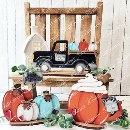 A rustic wooden chair displays autumn decor, featuring Janet's Craft Corner Fall Harvest Mini Shelf Sitters DIY kit—choose from 9 designs like a black truck with pumpkins, a white house, and signs reading “Pumpkin Patch” or “Farm Fresh Pumpkins.”.
