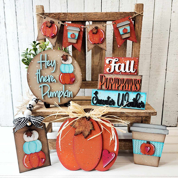 A rustic wooden chair is adorned with autumn-themed decorations from the Hello Pumpkin Decor Set by Janet's Craft Corner. The scene includes banners and signs featuring phrases like "Hey there, Pumpkin," "Fall," and "Sweater Weather." A to-go coffee cup and a heart complete this cozy home décor arrangement.