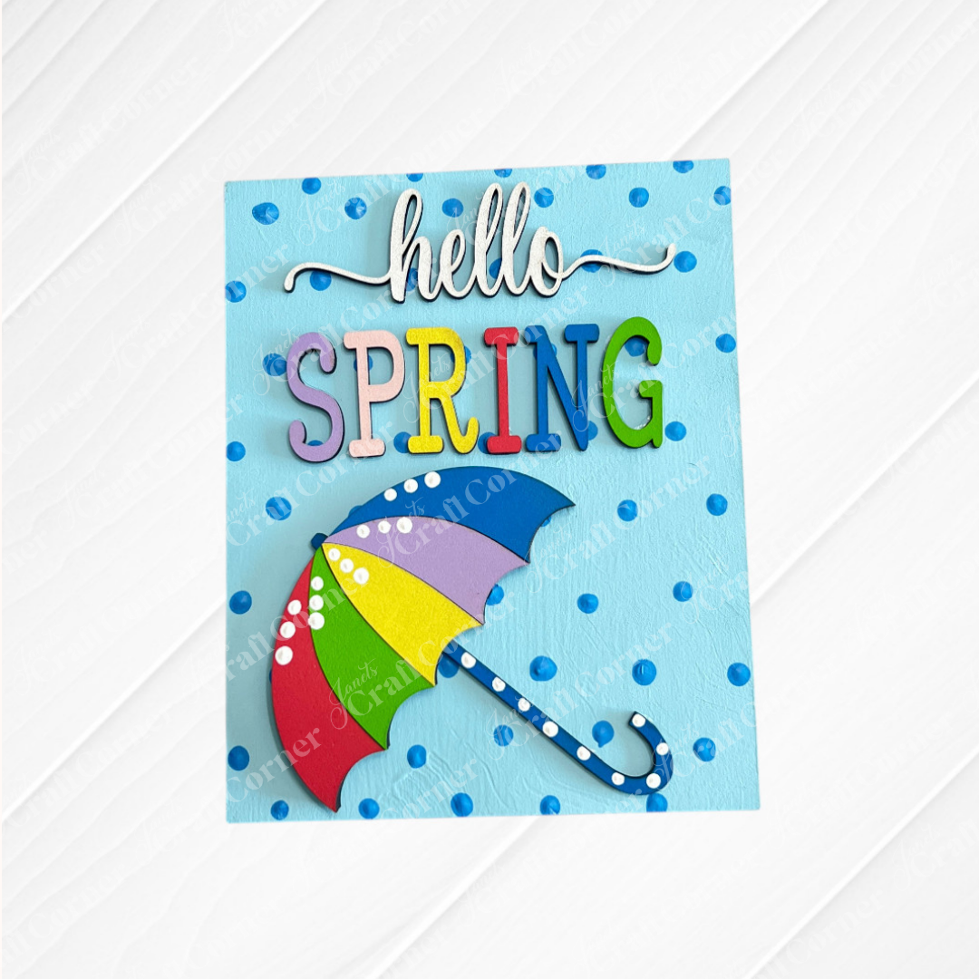 Add a splash of color to your tiered tray with Janet's Craft Corner's Spring Switchable Farmhouse Signs DIY Wood Decor Kit, featuring a vibrant "hello SPRING" card with a multicolored umbrella and blue polka dots on light blue.